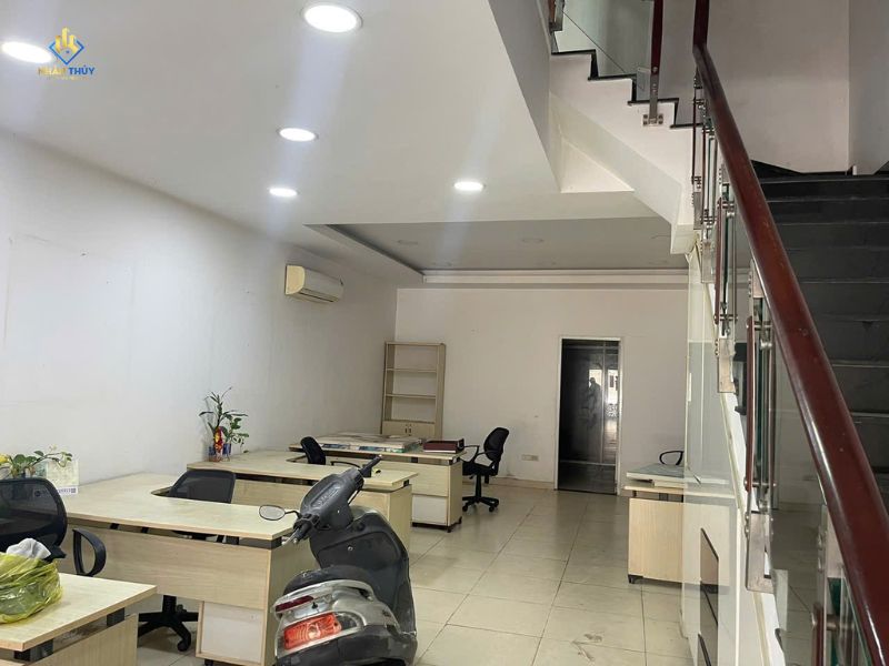 Không gian tầng trệt có tường trắng, bàn làm việc, xe máy và cầu thang