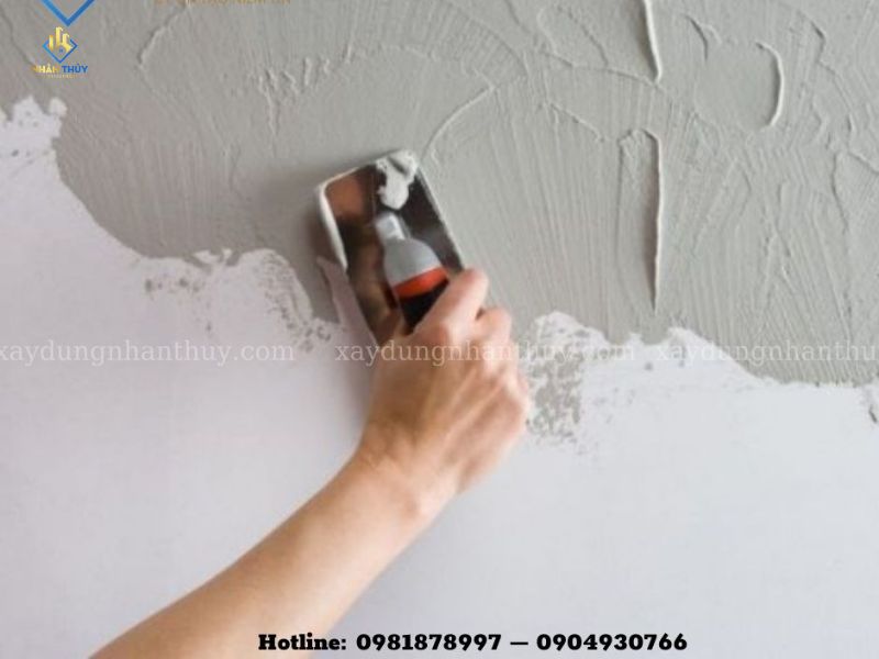 Cận cảnh tay người thợ dùng bay trét lớp bả lên tường