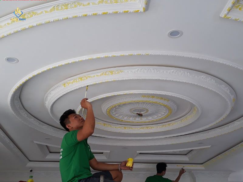 Người thợ dùng cọ tô màu vàng lên hoa văn phào chỉ trên trần trắng