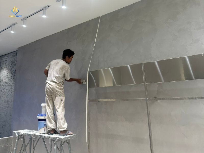 Người thợ dùng bay thi công trên mảng tường màu xám trong không gian nội thất
