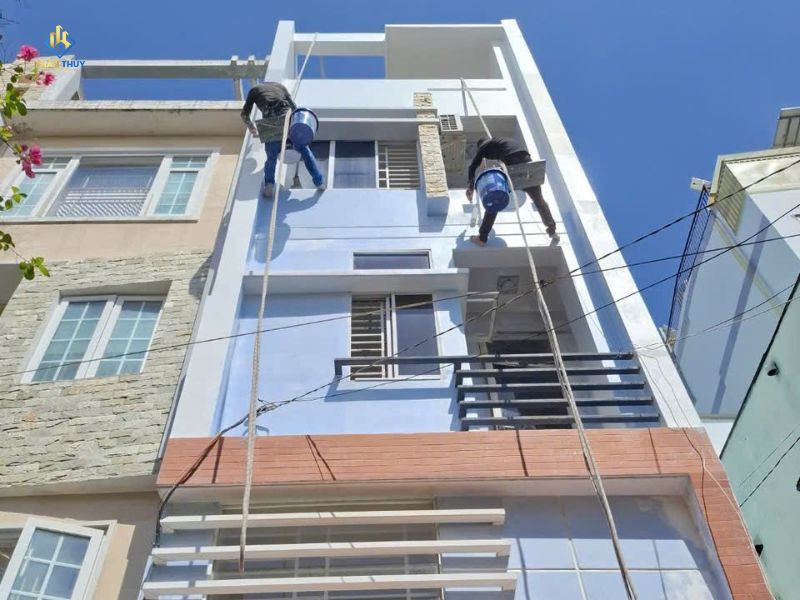 Hai thợ thi công bề mặt mặt tiền nhà trên cao bằng hệ dây treo