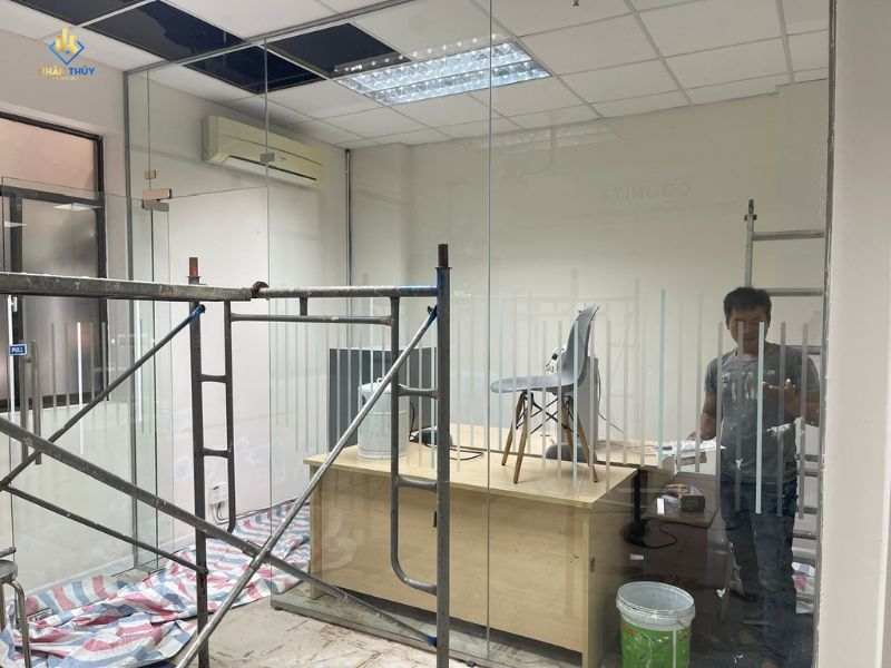 Thợ xử lý bề mặt tường trong phòng kính văn phòng trước khi sơn