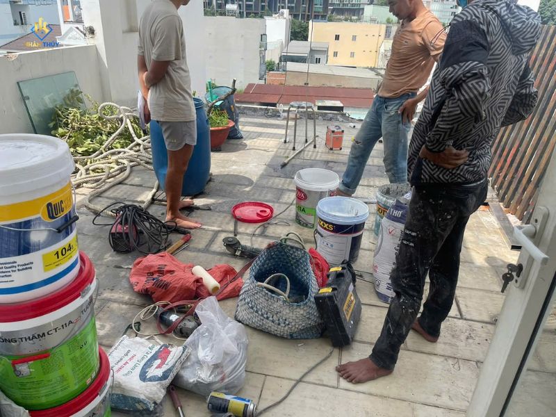 Thùng vật tư sơn và dụng cụ đặt trên sân thượng, cạnh nhóm người thi công